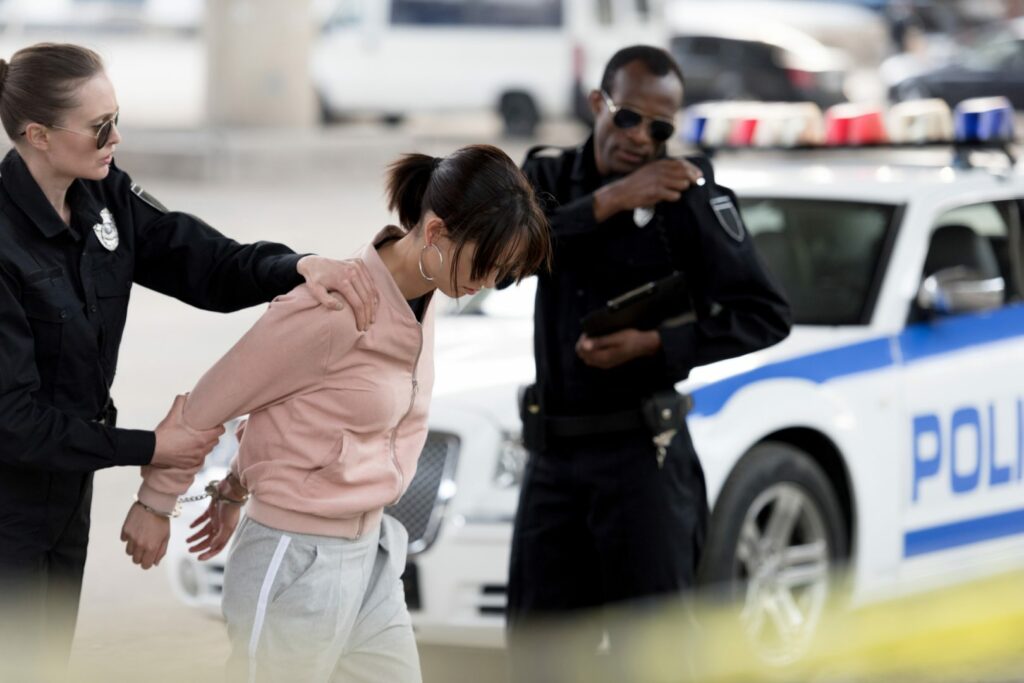 policewoman holding arrested young woman while her partner talking on portable radio