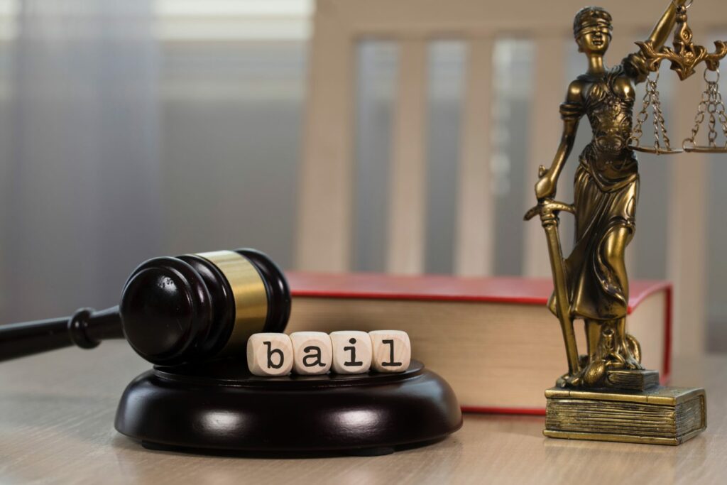 Word BAIL composed of wooden dices. Wooden gavel and statue of Themis in the background.