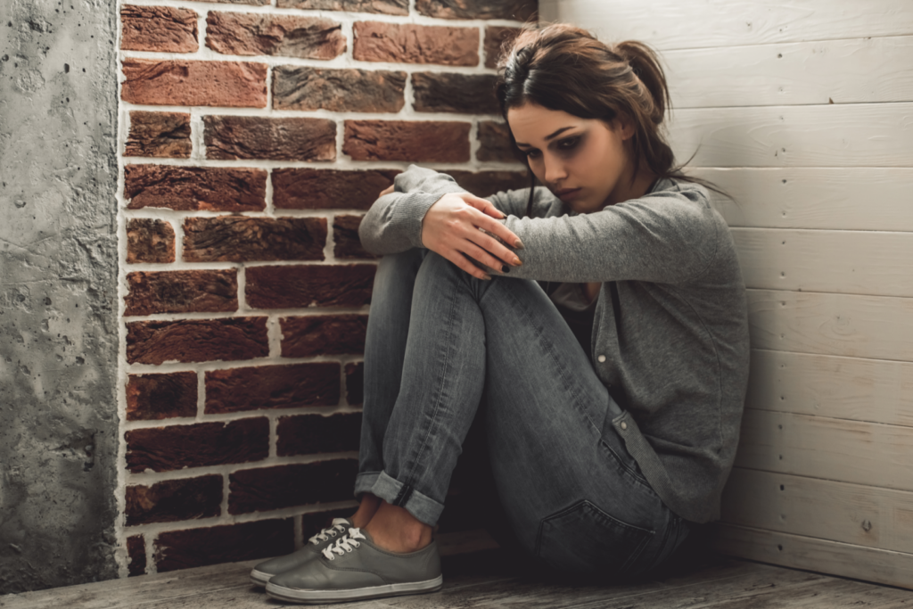 Portrait of young girl with bruises on her face looking sadly down while sitting on the floor